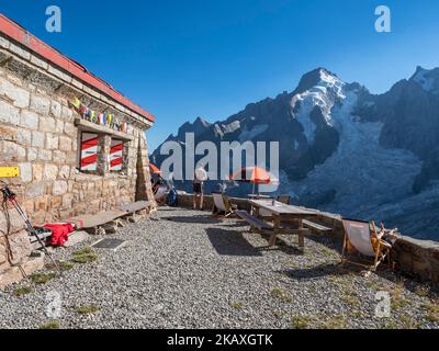 Refuge Cabane de l'UNE Neuve, touristes assis sur la terrasse, massif de l'aiguille rouges du Dolent à l'arrière, près de la Fouly, Val de Ferret, Suisse Banque D'Images