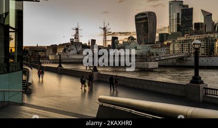 Les couples marchent le long de la promenade sur les rives de la Tamise London walkie-talkie et la ville dans le fond du HMS Belfast en premier plan la Tamise Londres Banque D'Images