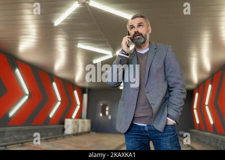 Un homme de cinquante ans du Caucase parle sur un téléphone portable dans un parking souterrain Banque D'Images