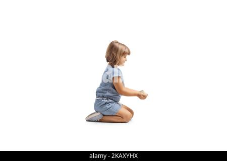 Photo de profil d'une petite fille tenant la nourriture de grain dans ses mains et s'agenouillant isolée sur fond blanc Banque D'Images