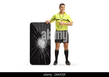 Portrait complet d'un arbitre de football pointant vers un smartphone écran cassé isolé sur fond blanc Banque D'Images