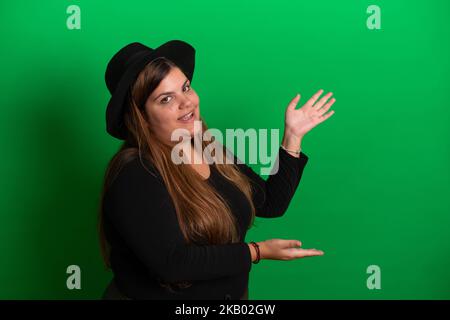 Jeune femme, portant un chapeau noir, gestes avec les mains le fond vert est facile à changer à n'importe quelle couleur Banque D'Images