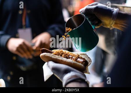 Chef tenant le hot dog tout en versant des oignons sur le hot dog, saucisse dans un rouleau, plus petit foyer peu profond, Banque D'Images