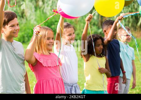 Joyeux préadolescents garçons et filles avec des ballons colorés sur la pelouse verte Banque D'Images