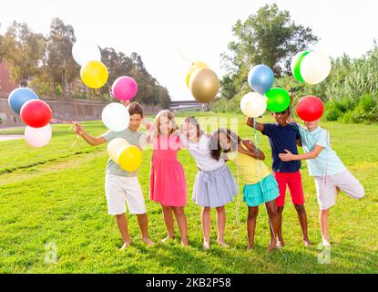 Joyeux préadolescents garçons et filles avec des ballons colorés sur la pelouse verte Banque D'Images
