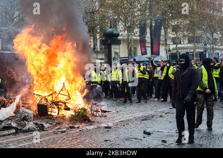 Paris, France, 24 novembre 2018. Les manifestants se tiennent devant un feu de meubles lors d'une manifestation contre les gilets jaunes (Gilets jaunes) contre la hausse des prix du pétrole et des coûts de la vie près de l'Arc de Triomphe sur les champs-Élysées. Les forces de sécurité à Paris ont tiré du gaz lacrymogène et du canon à eau pour disperser les manifestants. (Photo par Emeric Fohlen/NurPhoto) Banque D'Images