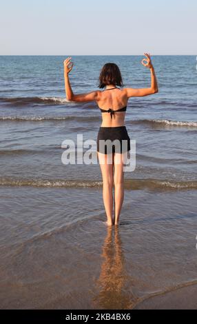 Jeune fille mince dos à dos tout en faisant des exercices de méditation de yoga et en faisant le symbole OM avec ses mains en été Banque D'Images