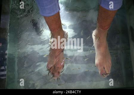 Un homme prend ses pieds en char rempli de poisson dans un bar et café de la ville de Gaza, en Palestine, sur 3 janvier 2019. Le chauffeur de café de Gaza a déclaré que son entreprise était en plein essor après le lancement du service de pédicure pour poissons dans la bande de Gaza assiégée. Une session de 30 minutes coûte environ $8 -- une somme énorme dans l'enclave côtière appauvrie. Mais des dizaines de personnes sont prêtes à payer le prix d'une fuite temporaire des conditions de vie difficiles à Gaza. (Photo de Majdi Fathi/NurPhoto) Banque D'Images