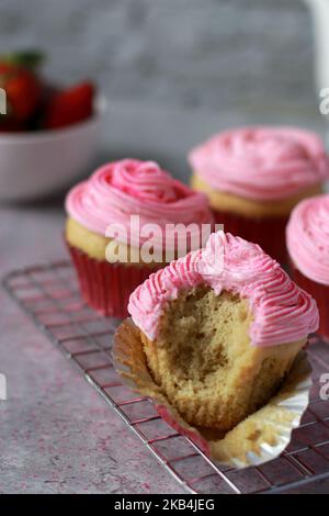 Gros plan d'un muffin mordu avec des arrosettes roses et de la crème au beurre sur la table en marbre gris Banque D'Images
