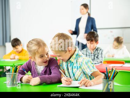 Les élèves heureux assis bavardant à leçon à l'école élémentaire Banque D'Images