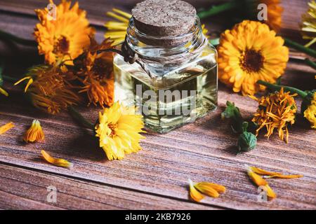Huile de calendula en bouteille de verre, Calendula officinalis , fleurs marigolées sur table en bois Banque D'Images