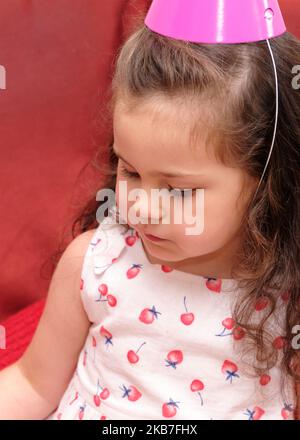 petite fille dans un chapeau de fête mangeant gâteau à la première fête d'anniversaire de son frère Banque D'Images