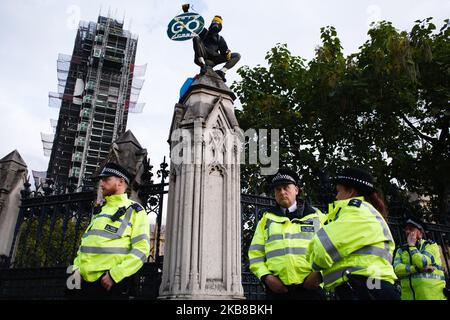 Un membre du mouvement activiste du changement climatique extinction Rebellion (XR), portant un masque à gaz et entouré de la police, présente sur le dessus du mur de la succession parlementaire à Londres, Angleterre, sur 15 octobre 2019. XR s'est engagé à poursuivre son « lion » de deux semaines dans la ville malgré que la police métropolitaine ait émis la nuit dernière une interdiction des actions de protestation du groupe, et a effacé son campement sur Trafalgar Square. (Photo de David Cliff/NurPhoto) Banque D'Images