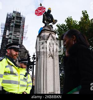 Un membre du mouvement activiste du changement climatique extinction Rebellion (XR), portant un masque à gaz et entouré de la police, présente sur le dessus du mur de la succession parlementaire à Londres, Angleterre, sur 15 octobre 2019. XR s'est engagé à poursuivre son « lion » de deux semaines dans la ville malgré que la police métropolitaine ait émis la nuit dernière une interdiction des actions de protestation du groupe, et a effacé son campement sur Trafalgar Square. (Photo de David Cliff/NurPhoto) Banque D'Images