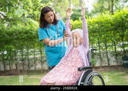 Médecin aide asiatique senior ou âgée vieille femme patiente exercice en fauteuil roulant avec heureux dans le parc. Banque D'Images