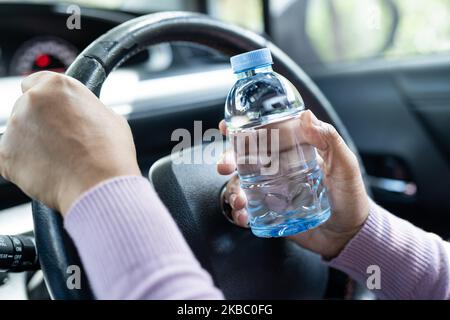 Femme asiatique chauffeur tenant une bouteille pour boire de l'eau tout en conduisant une voiture.Une bouteille d'eau chaude en plastique peut provoquer un incendie. Banque D'Images