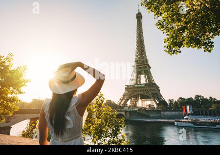 Jeune femme touriste en chapeau de soleil et robe blanche debout devant la Tour Eiffel à Paris au coucher du soleil. Voyage en France, concept de tourisme Banque D'Images