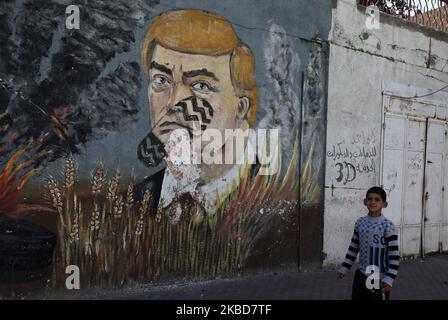 Un garçon marche à côté d'une fresque graffiti représentant le président américain Donald Trump avec un imprimé à chaussures sur son visage, à Gaza, sur 19 décembre 2019. (Photo de Majdi Fathi/NurPhoto) Banque D'Images