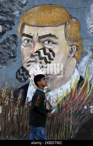 Un garçon marche à côté d'une fresque graffiti représentant le président américain Donald Trump avec un imprimé à chaussures sur son visage, à Gaza, sur 19 décembre 2019. (Photo de Majdi Fathi/NurPhoto) Banque D'Images