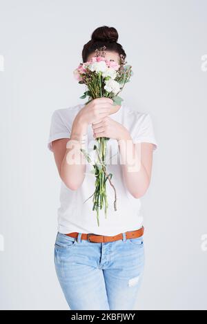 Il est facile de se cacher derrière de belles fleurs. Photo studio d'une femme méconnue couvrant son visage de fleurs sur fond gris. Banque D'Images