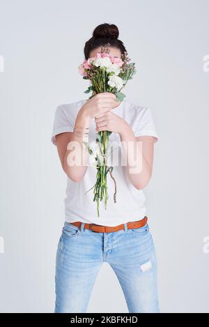 Restez fort tout en restant gentil. Photo studio d'une femme méconnue couvrant son visage de fleurs sur fond gris. Banque D'Images