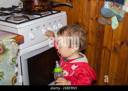 L'enfant joue sans surveillance dans la cuisine avec un poêle à gaz. Banque D'Images