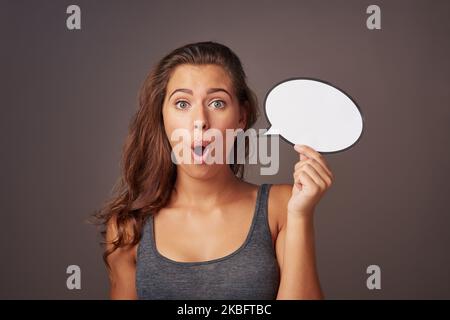 Vous n'y croiroirserez pas. Photo en studio d'une jeune femme attrayante tenant une bulle de parole vide et regardant choqué sur un fond gris. Banque D'Images