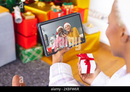 Femme afro-américaine avec des décorations de noël ayant appel vidéo avec heureux couple divers Banque D'Images