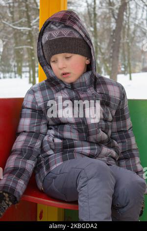 triste garçon assis dans le parc en hiver Banque D'Images