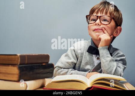 L'avenir appartient aux curieux. Studio photo d'un petit garçon intelligent lisant des livres et regardant réfléchi sur un fond gris. Banque D'Images