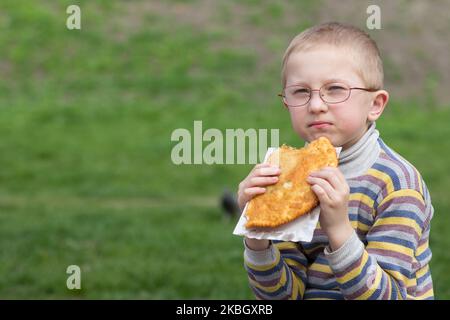 Garçon avec des verres mangeant Chebureau sur un fond d'herbe Banque D'Images