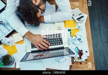 C'était une journée longue et écrasante. Photo en grand angle d'un jeune homme d'affaires avec sa tête abaissée sur un bureau. Banque D'Images