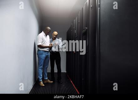 Équipement essentiel. Prise de vue en longueur de deux techniciens INFORMATIQUES utilisant une tablette numérique tout en travaillant dans un centre de données. Banque D'Images