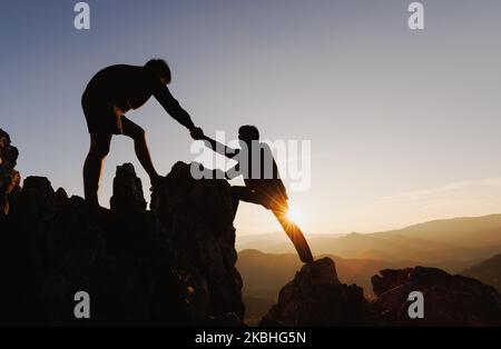 Silhouette de deux personnes grimpant sur la falaise de montagne et l'une d'entre elles donnant la main utile. Concept de travail d'équipe et d'aide aux personnes. Banque D'Images