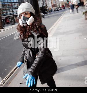 Une femme porte un masque respiratoire et des gants en latex sur une route de Tottenham court presque déserte à Londres, en Angleterre, sur 21 mars 2020. Une grande partie du centre de Londres était pratiquement vide aujourd’hui, un jour après que le Premier ministre britannique Boris Johnson ait ordonné la fermeture de tous les pubs, bars, cafés et restaurants du pays. Cette décision constitue un renforcement des mesures visant à faire respecter la « distanciation sociale » qui est pressée pour les citoyens de réduire la croissance des infections au coronavirus covid-19. Des boîtes de nuit, des théâtres, des cinémas, des salles de sport et des centres de loisirs ont également été commandés fermés. Quelques boutiques dans le centre de la capitale remai Banque D'Images