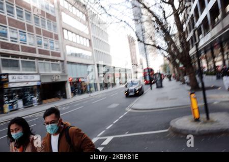 Un couple portant des masques se promène le long d'une route près déserte de Tottenham court à Londres, en Angleterre, sur 21 mars 2020. Une grande partie du centre de Londres était pratiquement vide aujourd’hui, un jour après que le Premier ministre britannique Boris Johnson ait ordonné la fermeture de tous les pubs, bars, cafés et restaurants du pays. Cette décision constitue un renforcement des mesures visant à faire respecter la « distanciation sociale » qui est pressée pour les citoyens de réduire la croissance des infections au coronavirus covid-19. Des boîtes de nuit, des théâtres, des cinémas, des salles de sport et des centres de loisirs ont également été commandés fermés. Quelques magasins dans le centre de la capitale sont restés ouverts aujourd'hui, al Banque D'Images