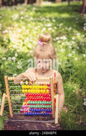 jolie petite fille assise dans la forêt verte de printemps et comptant à abacus Banque D'Images