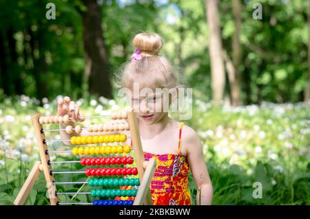 jolie petite fille assise dans la forêt verte de printemps et comptant à abacus Banque D'Images