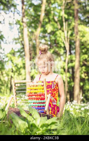 jolie petite fille assise dans la forêt verte de printemps et comptant à abacus Banque D'Images