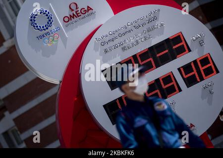 Les personnes qui portent des masques protecteurs en raison de l'épidémie de coronavirus (COVID 19) marchent sur des aiguilles d'une horloge Omega, Qui était précédemment utilisé comme compte à rebours pour les Jeux Olympiques de Tokyo 2020 et qui affiche actuellement l'heure et la date actuelles, après l'annonce du report des Jeux à l'été 2021, à Tokyo, Japon, 25 mars 2020. (Photo par Alessandro Di Ciommo/NurPhoto) Banque D'Images