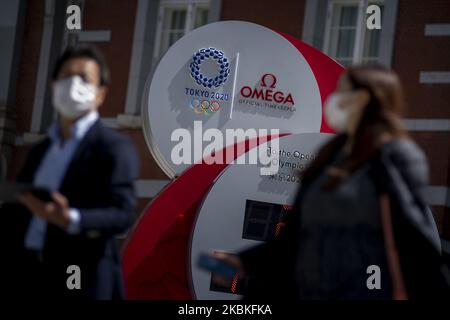 Les personnes qui portent des masques protecteurs en raison de l'épidémie de coronavirus (COVID 19) marchent sur des aiguilles d'une horloge Omega, Qui était précédemment utilisé comme compte à rebours pour les Jeux Olympiques de Tokyo 2020 et qui affiche actuellement l'heure et la date actuelles, après l'annonce du report des Jeux à l'été 2021, à Tokyo, Japon, 25 mars 2020. (Photo par Alessandro Di Ciommo/NurPhoto) Banque D'Images