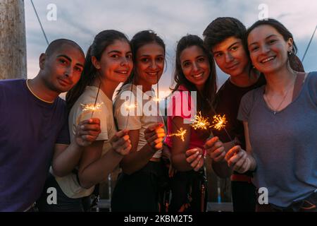 Jeune groupe de grimpeurs de rock qualifiés ayant du plaisir et jouant avec des sparkles avec le coucher du soleil en arrière-plan Banque D'Images