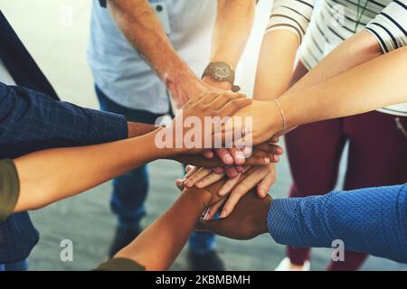 Mettez-le dans les gars. Un groupe de personnes méconnaissables mettant leurs mains ensemble dans un caucus à côté d'un bâtiment. Banque D'Images