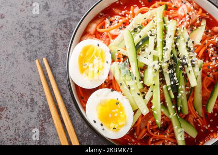 Salade de nouilles épicées coréennes Bibim-guksu avec kimchi, concombre et oeufs dans le bol de la table. Vue horizontale du dessus Banque D'Images