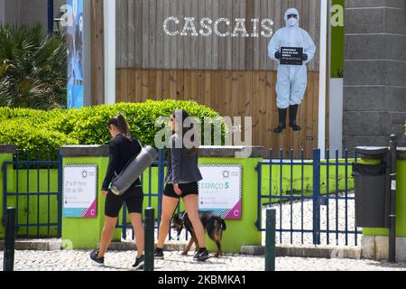 Deux femmes marchent près d'une annonce de prévention COVID-19, placée dans une rue de la ville de Caiscais, Portugal, Portugal, Portugal, 19 avril 2020. Au cours de la période d'urgence due à la COVID-19, le Portugal renforce ses mesures sanitaires pour prévenir d'autres épidémies. L'utilisation obligatoire de masques de protection et la découpe temporaire des plages et des zones publiques font partie de ses nouvelles mesures visant à contenir la pandémie. (Photo par Jorge Mantilla/NurPhoto) Banque D'Images