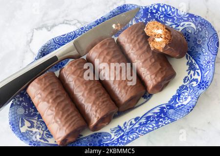 Rouleaux individuels de éponge de chocolat sur un plat bleu et blanc à motifs avec un couteau de service. Sur fond de marbre blanc Banque D'Images