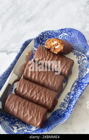 Rouleaux individuels de éponge de chocolat sur un plat bleu et blanc à motifs avec un couteau de service. Sur fond de marbre blanc Banque D'Images