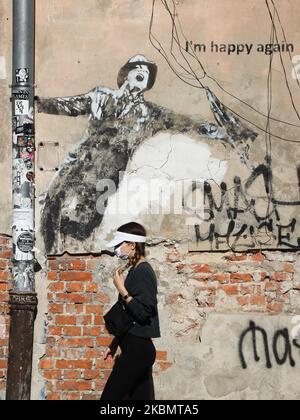 Une femme portant un masque facial protecteur en raison de la propagation du coronavirus, marche à côté du graffiti « Je suis heureux à nouveau » dans le quartier Kazimierz de Cracovie, en Pologne, sur 23 avril 2020. La règle de la couverture du nez et de la bouche dans les lieux publics avec des masques faciaux, des charves ou des mouchoirs est entrée en vigueur à partir de 16 avril. L'ordonnance ne s'applique pas aux enfants jusqu'à l'âge de deux ans et aux personnes qui ne peuvent pas couvrir leur bouche ou leur nez en raison de difficultés respiratoires. (Photo de Beata Zawrzel/NurPhoto) Banque D'Images