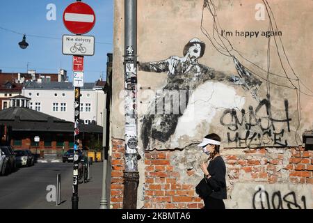 Une femme portant un masque facial protecteur en raison de la propagation du coronavirus, marche à côté du graffiti « Je suis heureux à nouveau » dans le quartier Kazimierz de Cracovie, en Pologne, sur 23 avril 2020. La règle de la couverture du nez et de la bouche dans les lieux publics avec des masques faciaux, des charves ou des mouchoirs est entrée en vigueur à partir de 16 avril. L'ordonnance ne s'applique pas aux enfants jusqu'à l'âge de deux ans et aux personnes qui ne peuvent pas couvrir leur bouche ou leur nez en raison de difficultés respiratoires. (Photo de Beata Zawrzel/NurPhoto) Banque D'Images