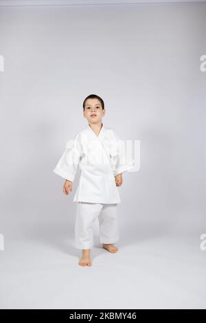 Un petit garçon dans un kimono pratique le karaté sur fond blanc. Banque D'Images